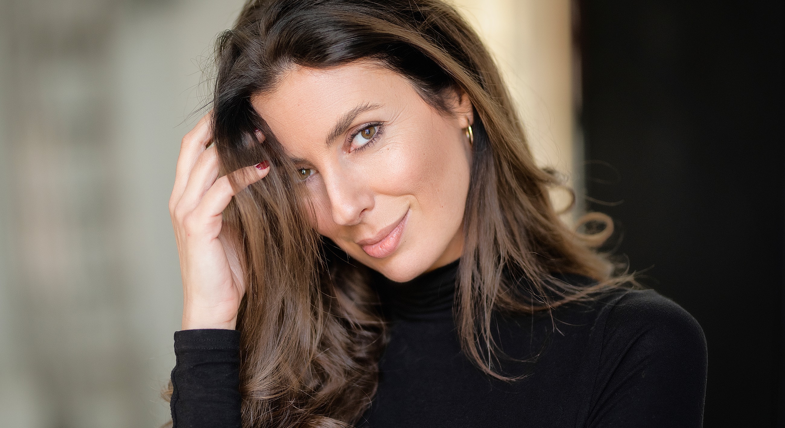 Woman smiling and touching her hair lightly.