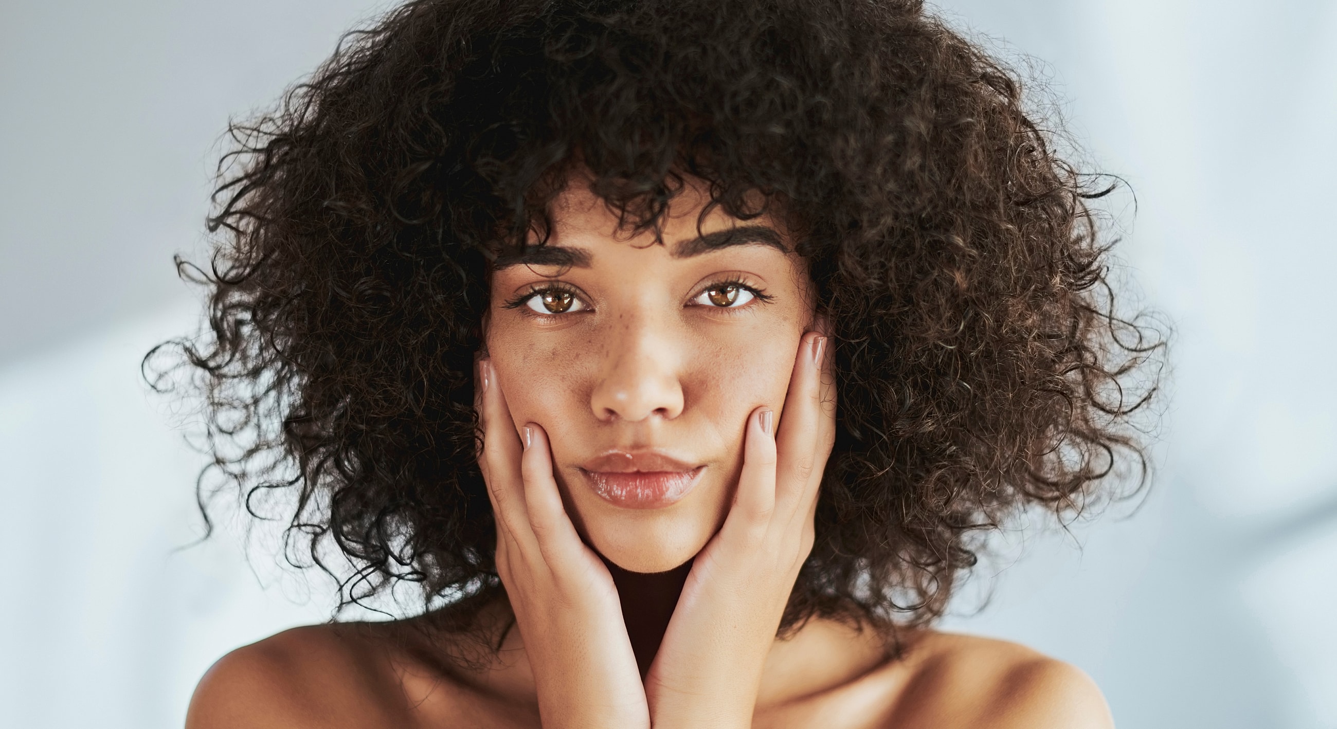 Woman with curly hair holding her face.